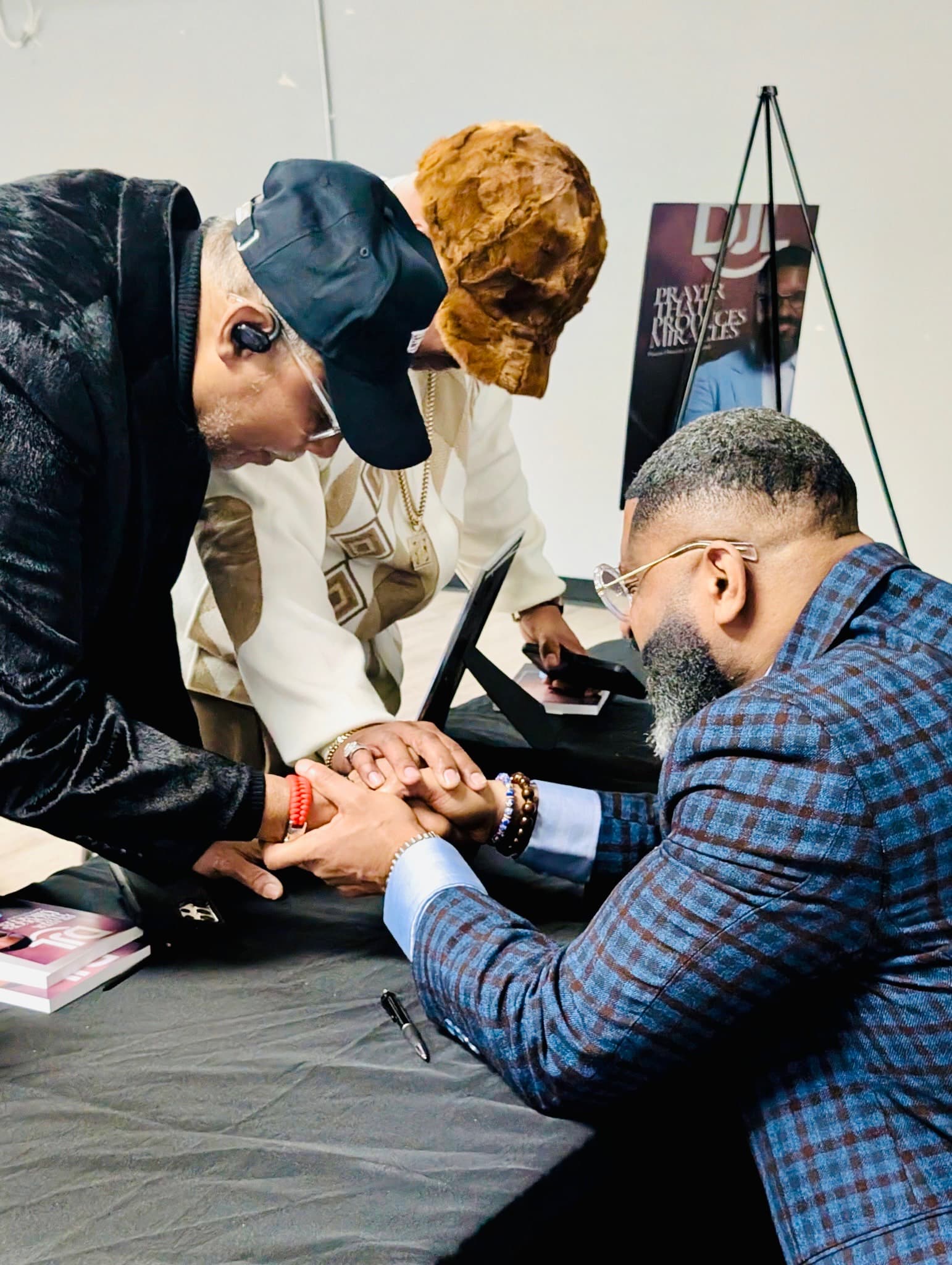 Three men lean over a table and clasp hands together in a shared prayer.