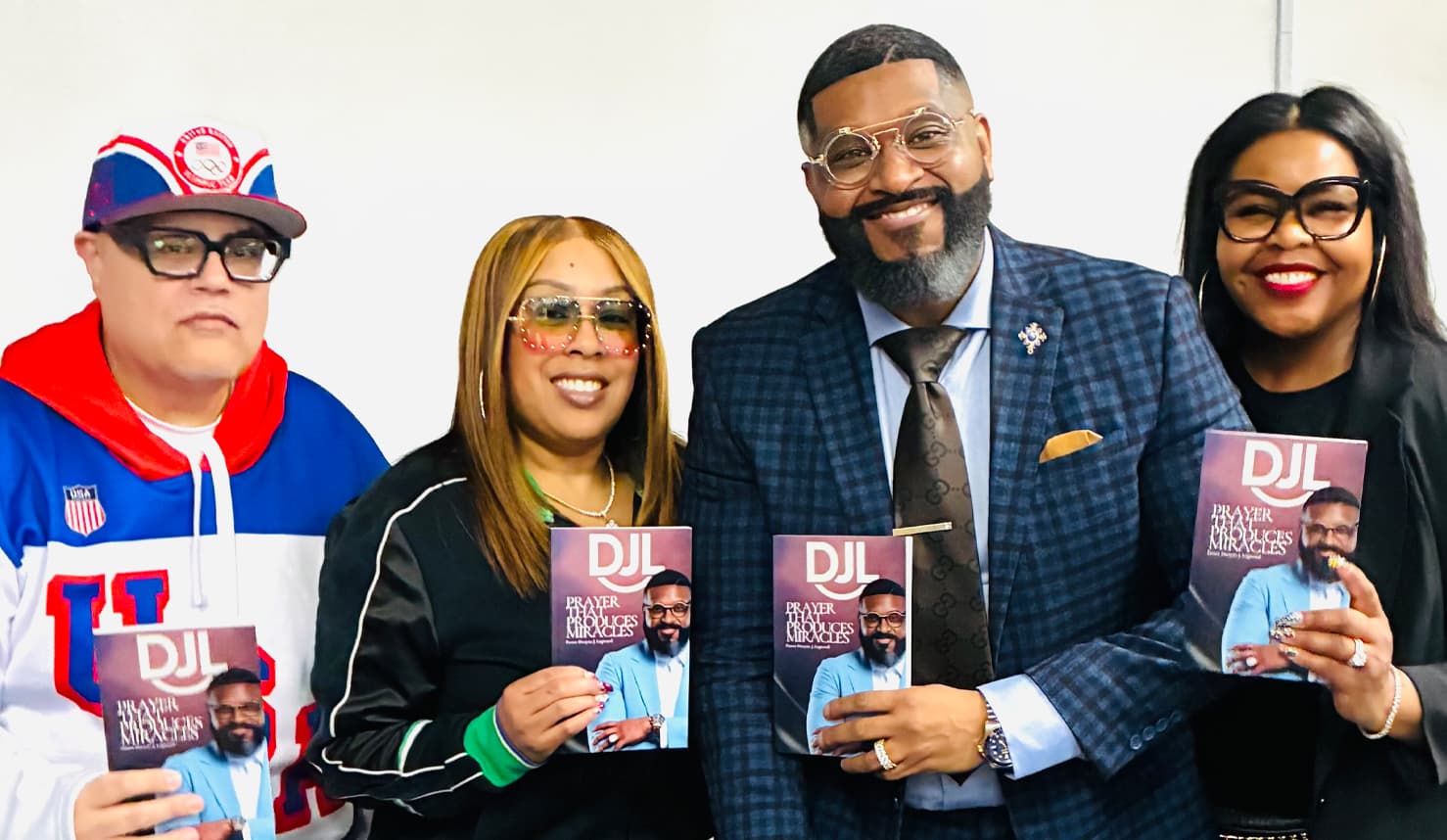 Four people posing while holding copies of the book DJL: Prayer That Produces Miracles.