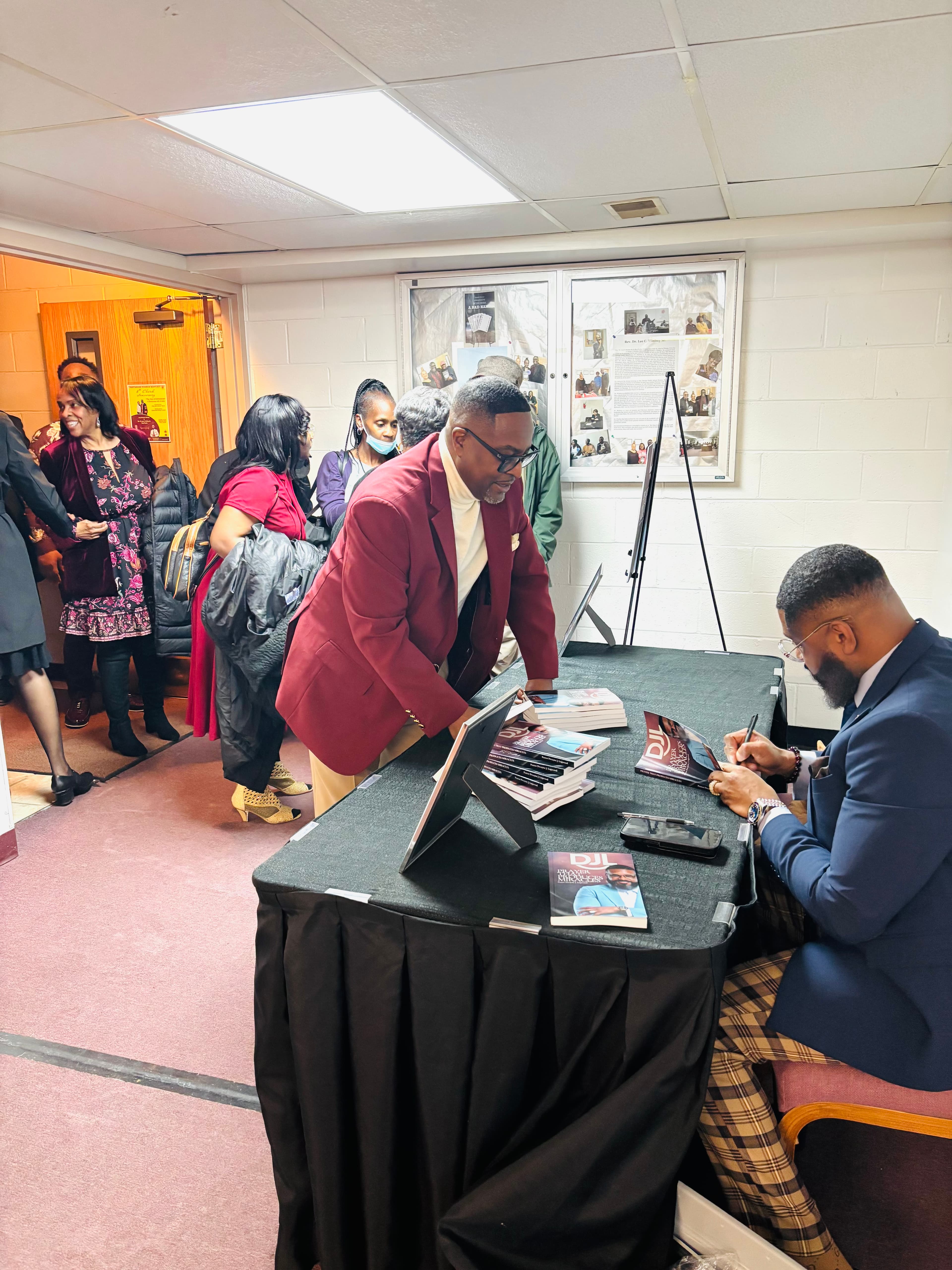 Man in blue suit signs books for a line of people at a draped table.